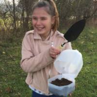 Student holds shovel and container of soil
